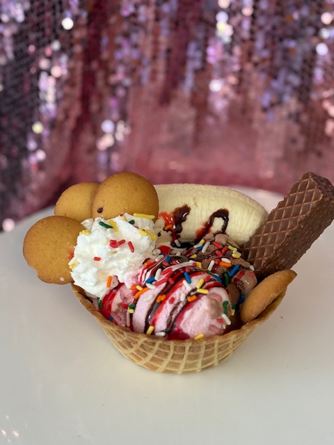 Banana split sundae in a waffle bowl with sprinkles and vanilla wafers.