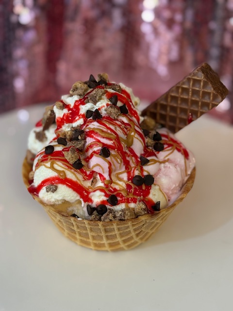 Strawberry sundae in a waffle bowl with chocolate chips, caramel drizzle, and a wafer cookie.